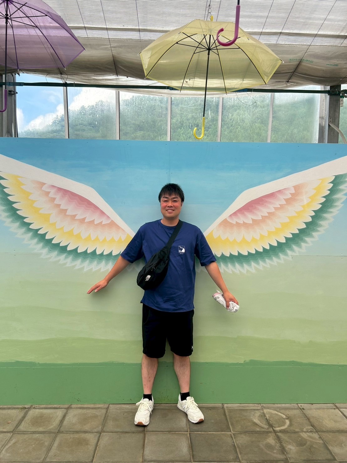 色鮮やかな翼の壁画の前に立つ砂壁進策さん